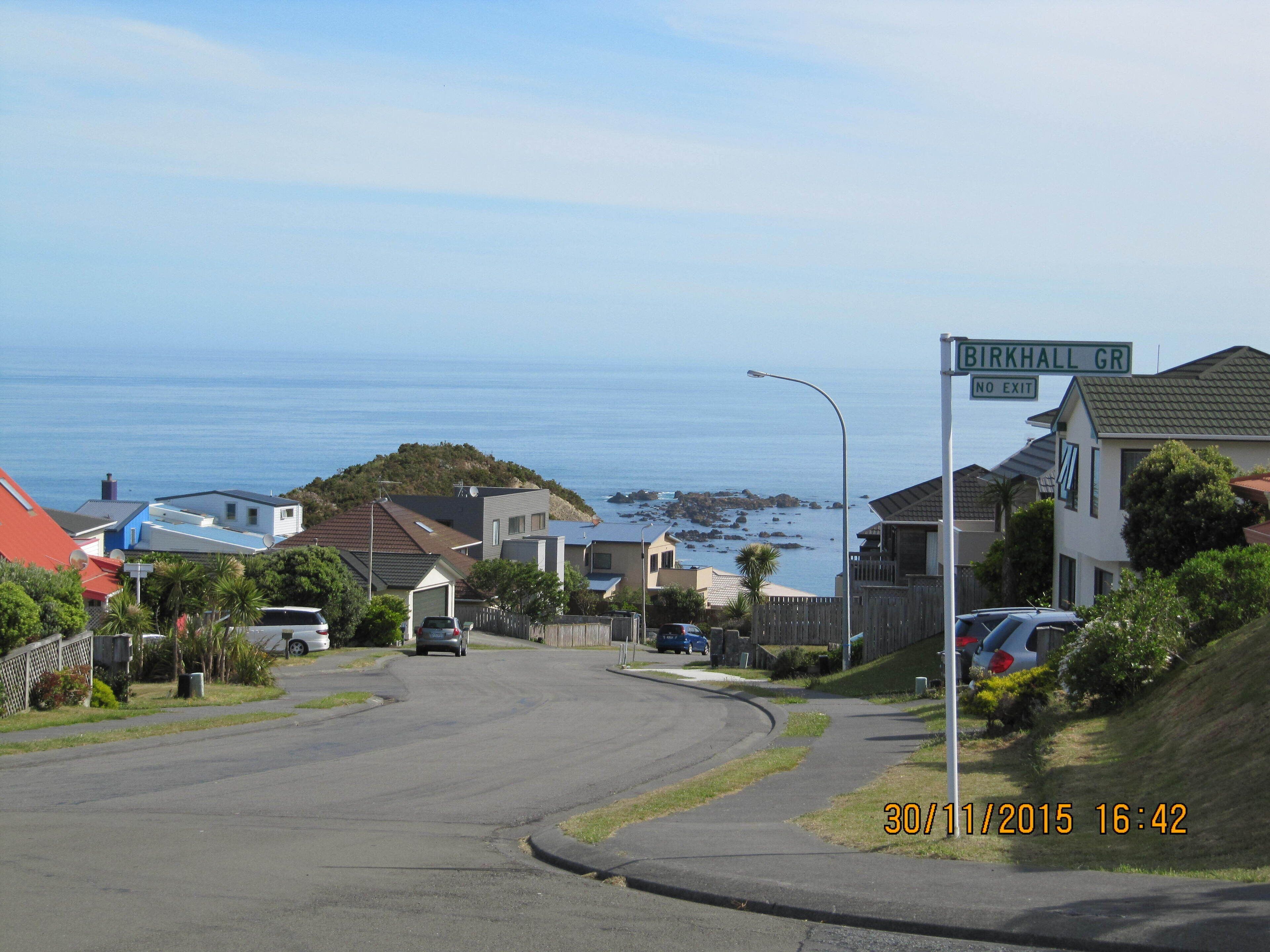 A residential street with houses, a 'No Exit' sign, and a view of the ocean.