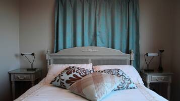Un dormitorio con una cama, dos mesitas de noche, una lámpara sobre cada una y una cortina.