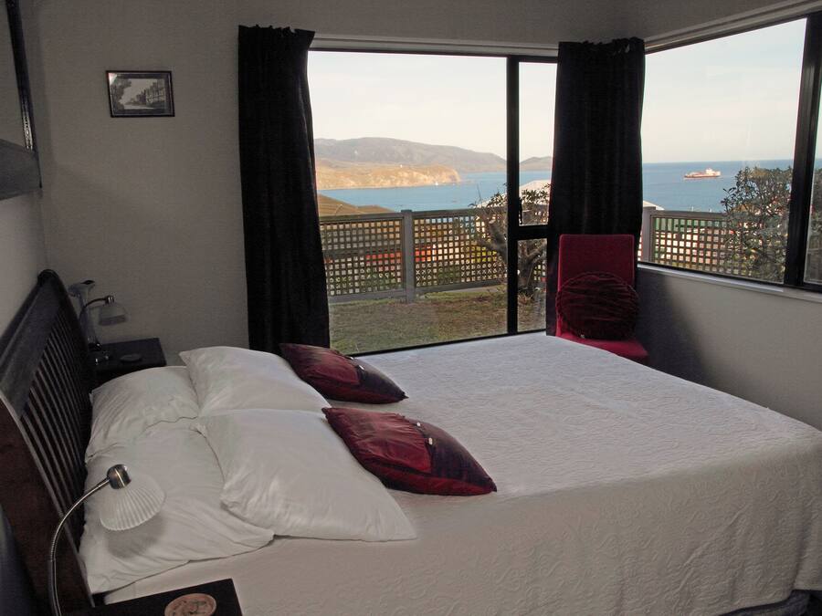 A bedroom with a large bed, a nightstand, a lamp, and a view of the sea and hills.