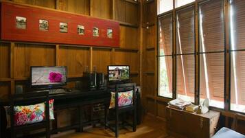 A room with wooden paneling, a desk with two monitors, a chair with a floral cushion, and a window with shutters.