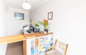 A reception desk with a wooden counter, a chair, and a bulletin board with various pamphlets. - Kaitaia Motor Lodge (Kaitaia)