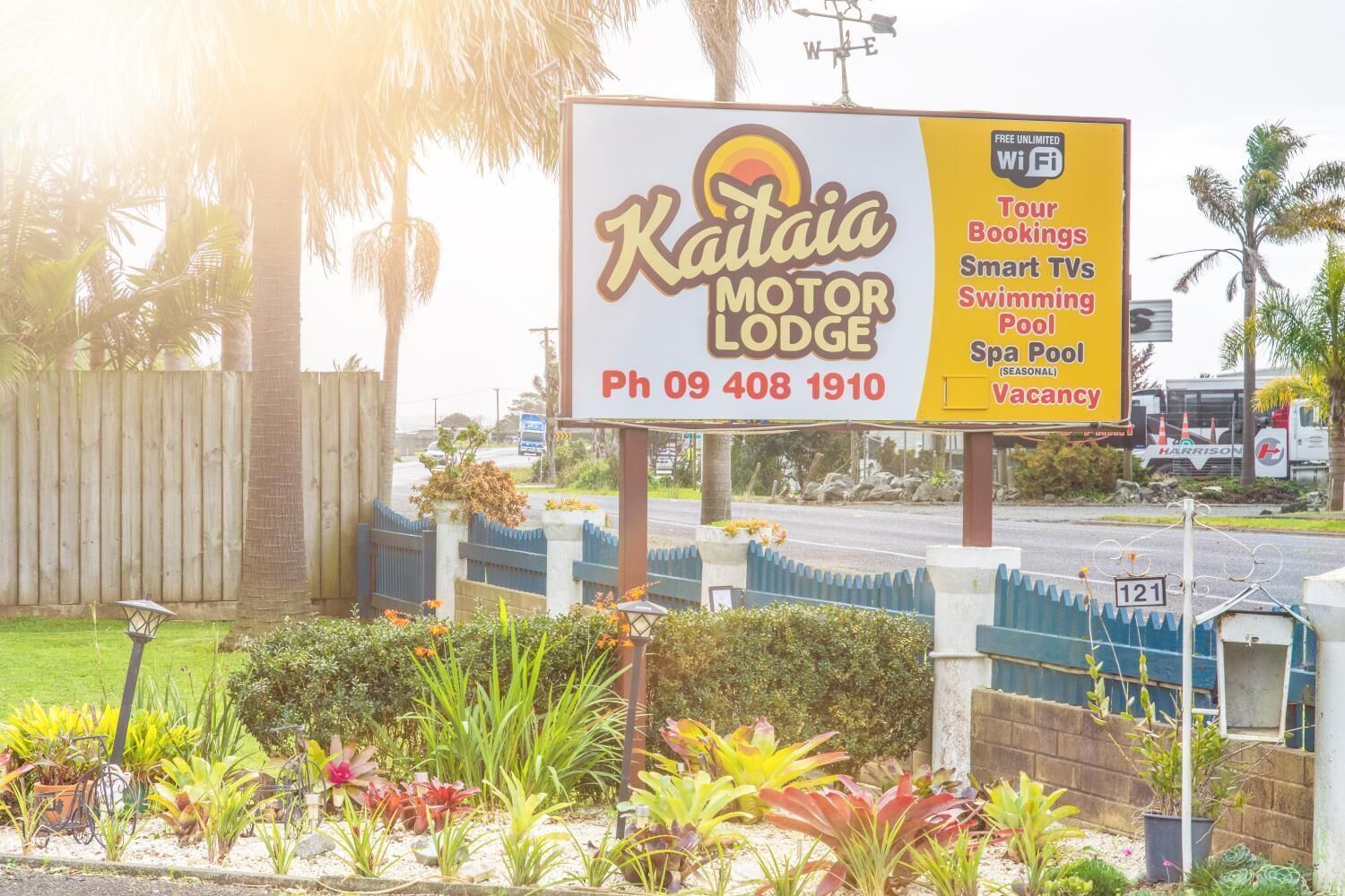 A sign for Kaitai Motor Lodge advertising amenities like tour bookings, smart TVs, a swimming pool, and a spa pool.