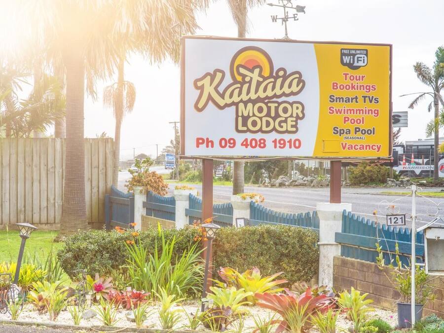 A sign for Kaitai Motor Lodge advertising amenities like tour bookings, smart TVs, a swimming pool, and a spa pool.