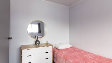 A bedroom with a bed, a dresser with drawers, a round mirror, and a white door.