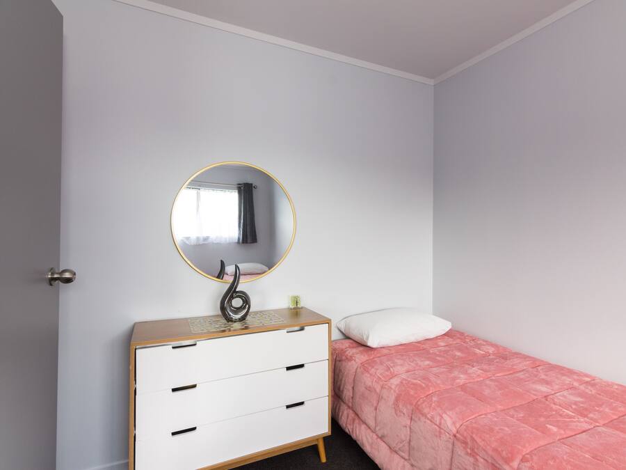 A bedroom with a bed, a dresser with drawers, a round mirror, and a white door.