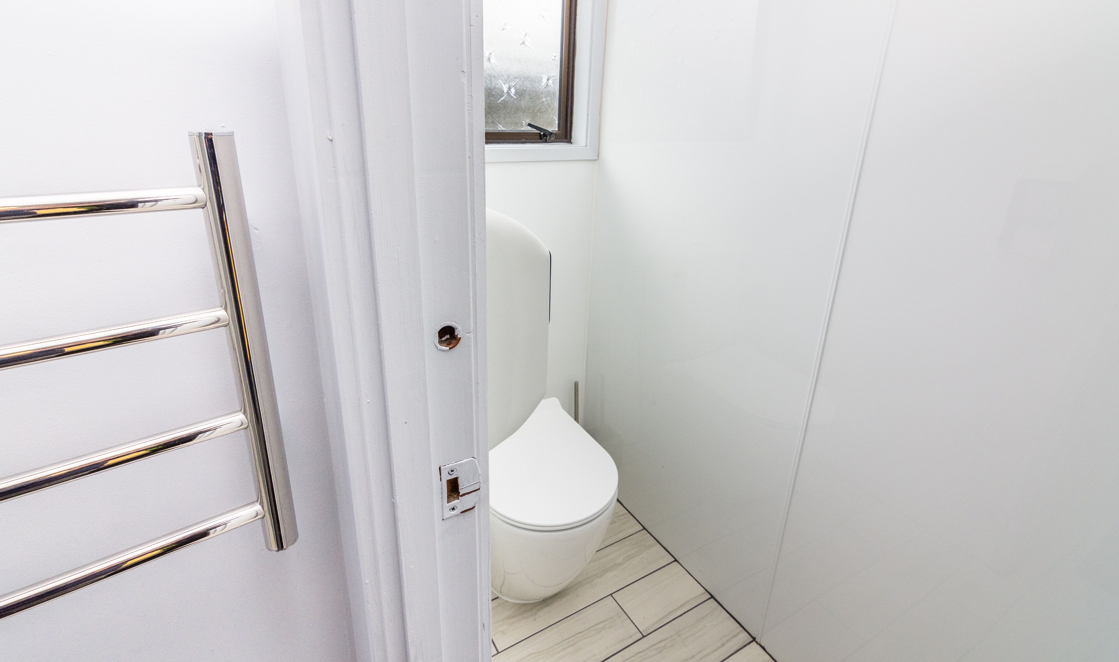 A small, narrow bathroom with a white toilet, a door with a silver handle, and a window with frosted glass.