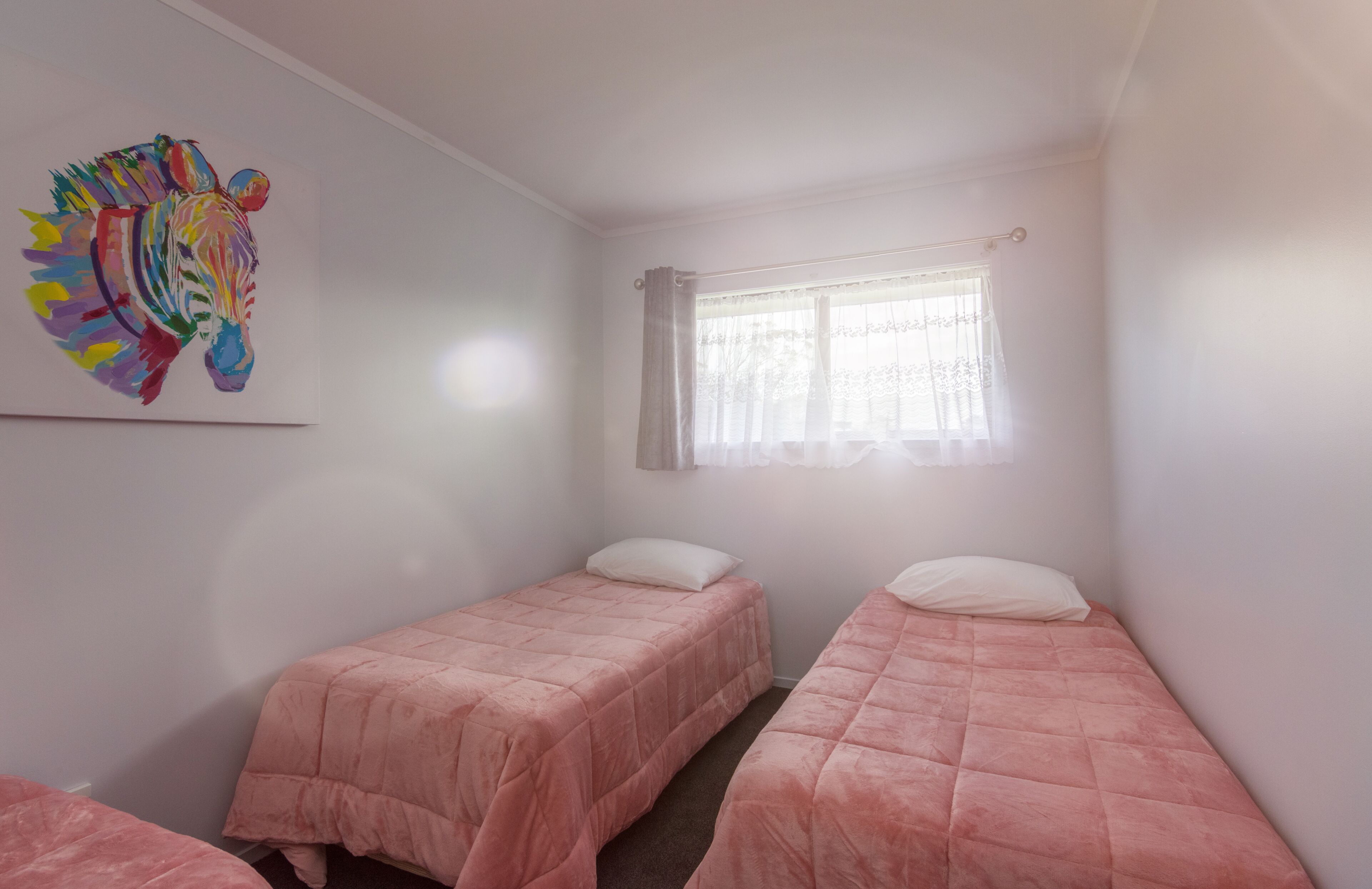 A room with two beds, a window with sheer curtains, and a colorful abstract painting on the wall.