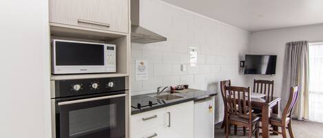 Una cocina moderna con armarios blancos, microondas integrado, horno y comedor con mesa y sillas.