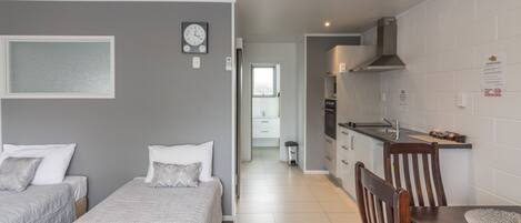 Una habitación de hotel moderna con dos camas, una kitchenette, un comedor y un baño.