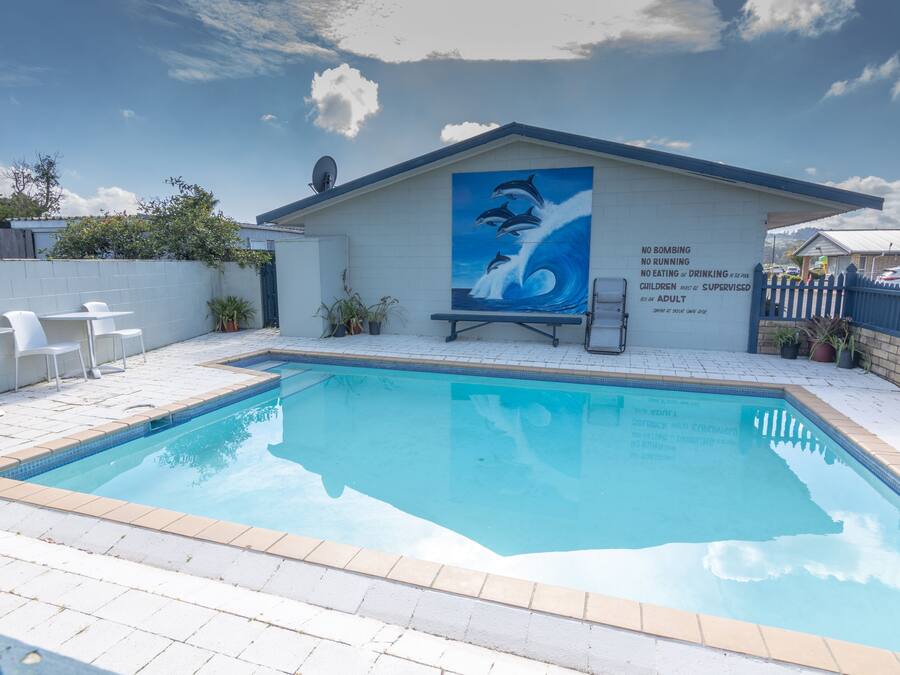 A swimming pool with a mural of dolphins, a white fence, and a bench.