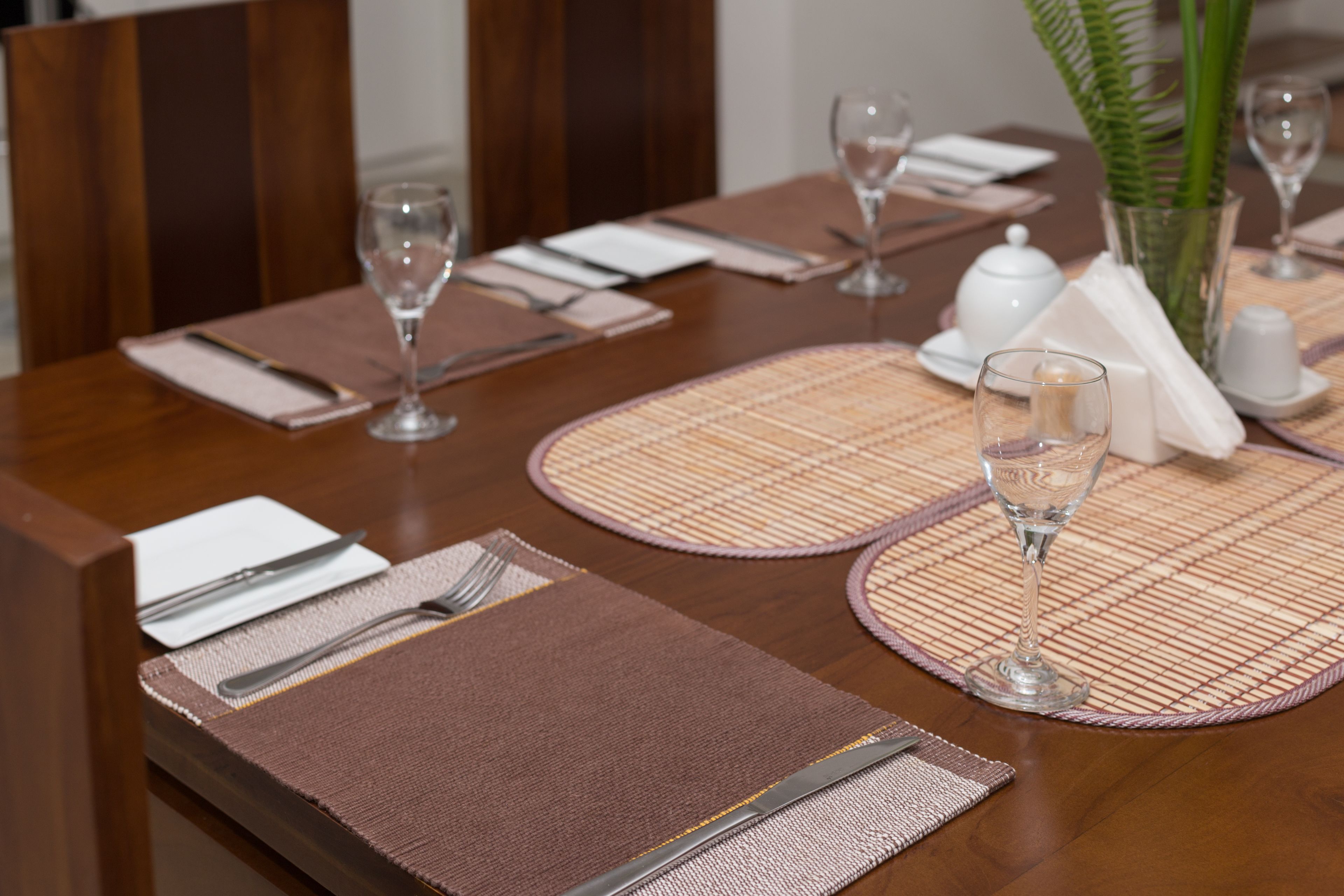 Une table à manger dressée avec des sets de table, des couverts et des verres à vin.