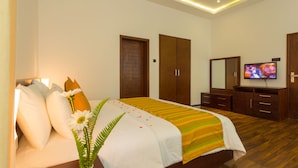 Una habitación de hotel moderna con una cama grande, televisor, muebles de madera y un espejo.