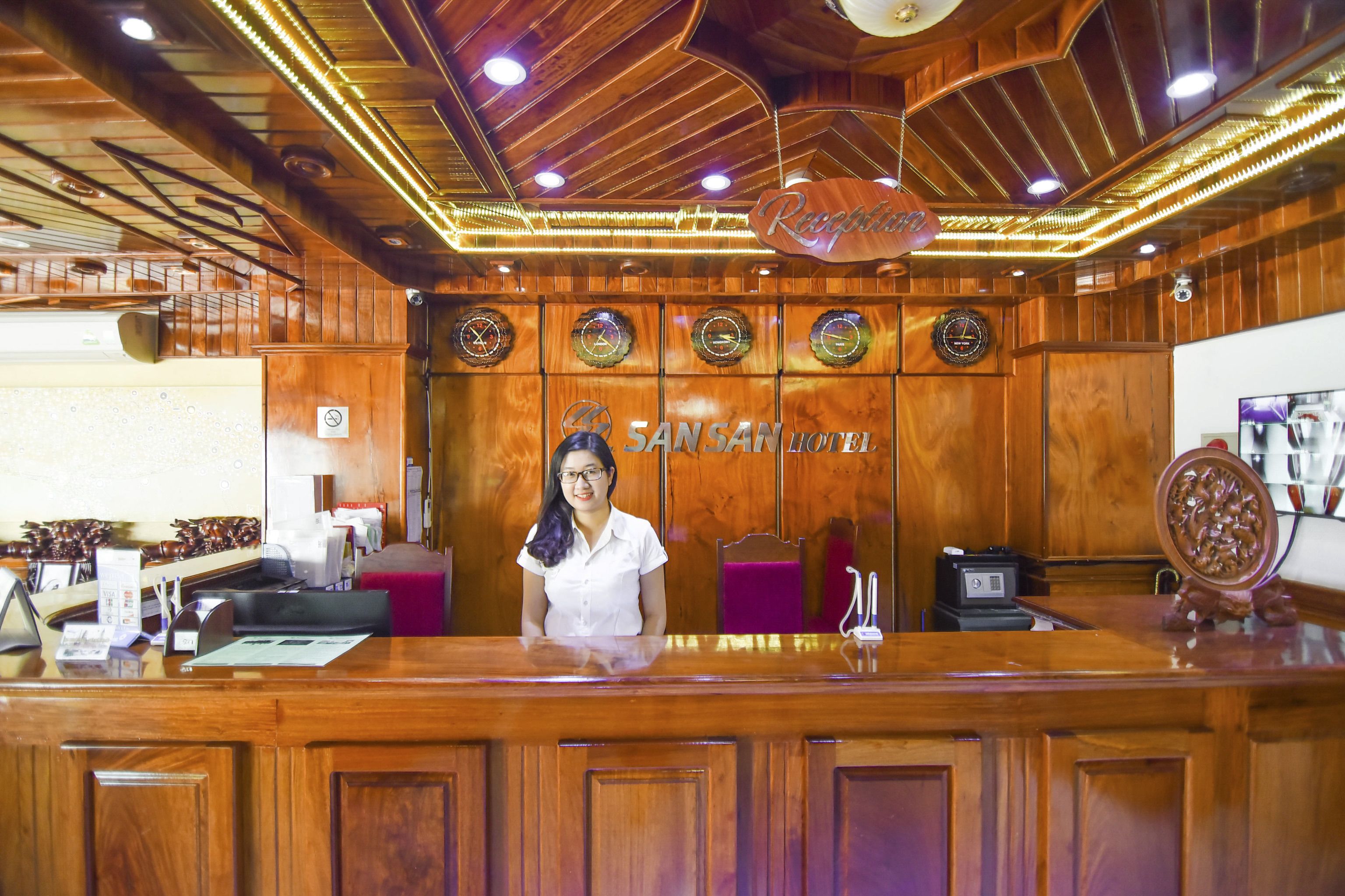 A reception desk with a wooden finish, a reception area, and a sign that reads "SAN SAN HOTEL".