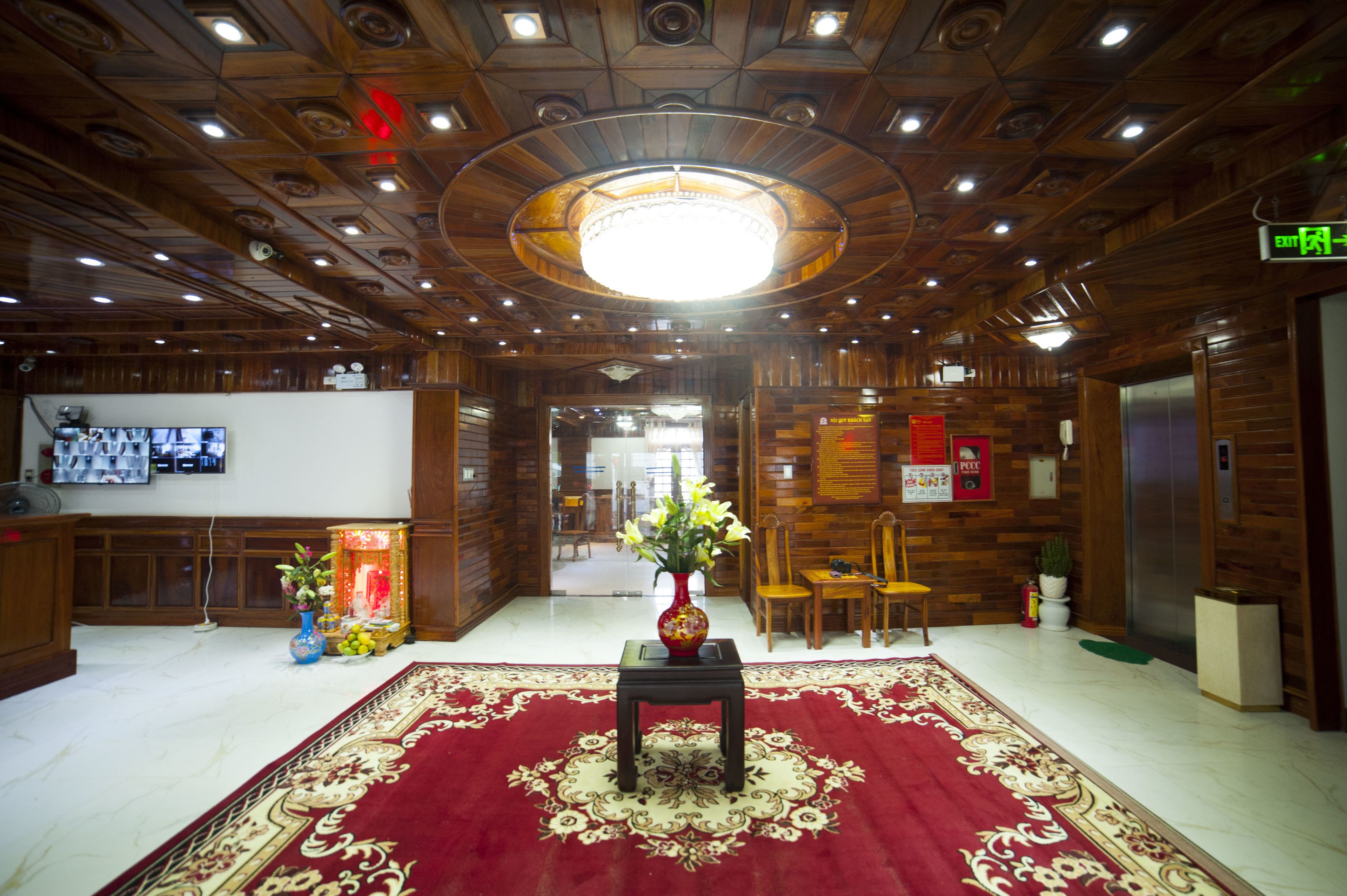 A lobby with a wooden ceiling, a chandelier, a red carpet, and a reception desk with a television.