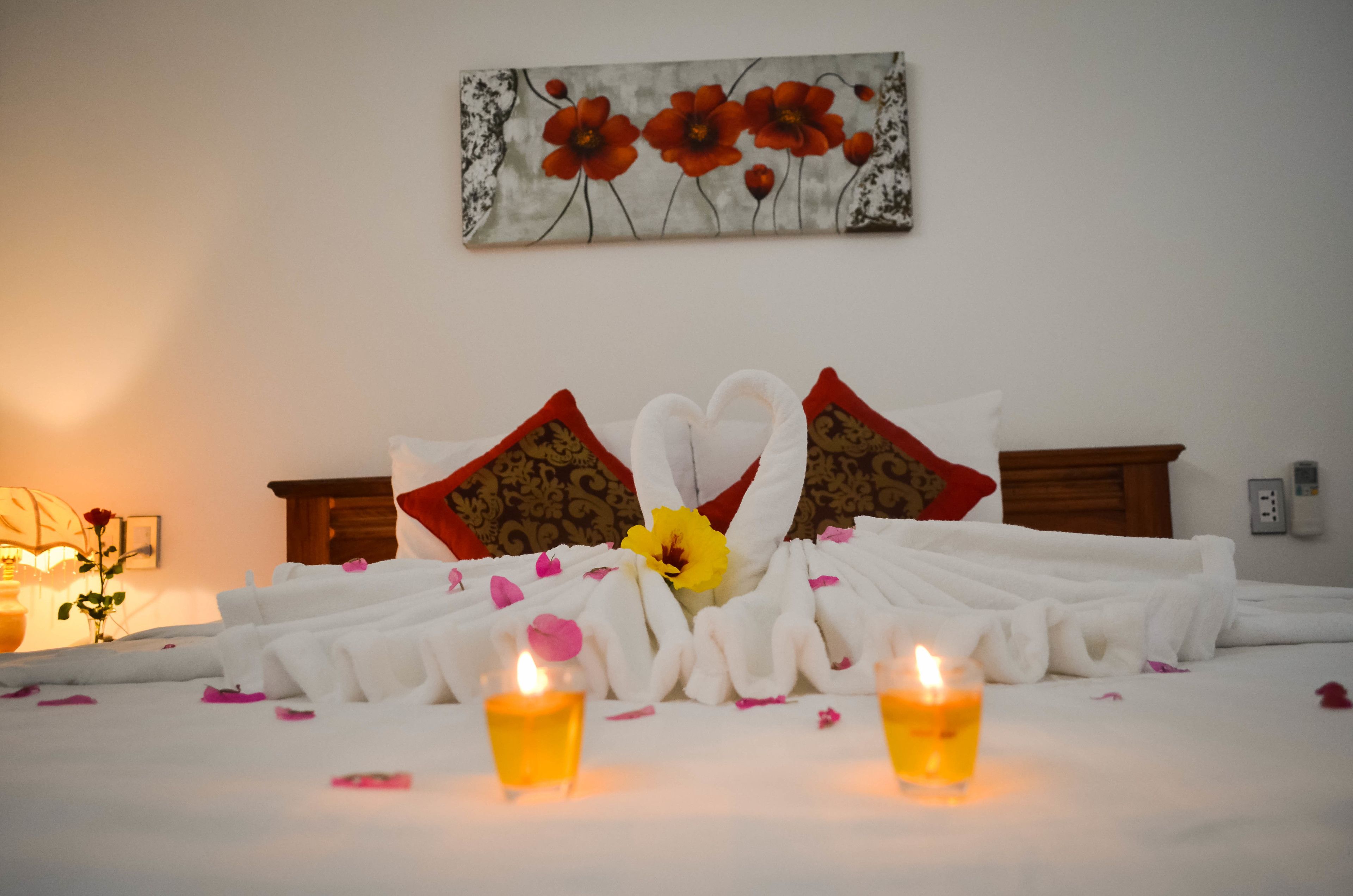 A neatly made bed with white linens, two candles, and a decorative flower arrangement.