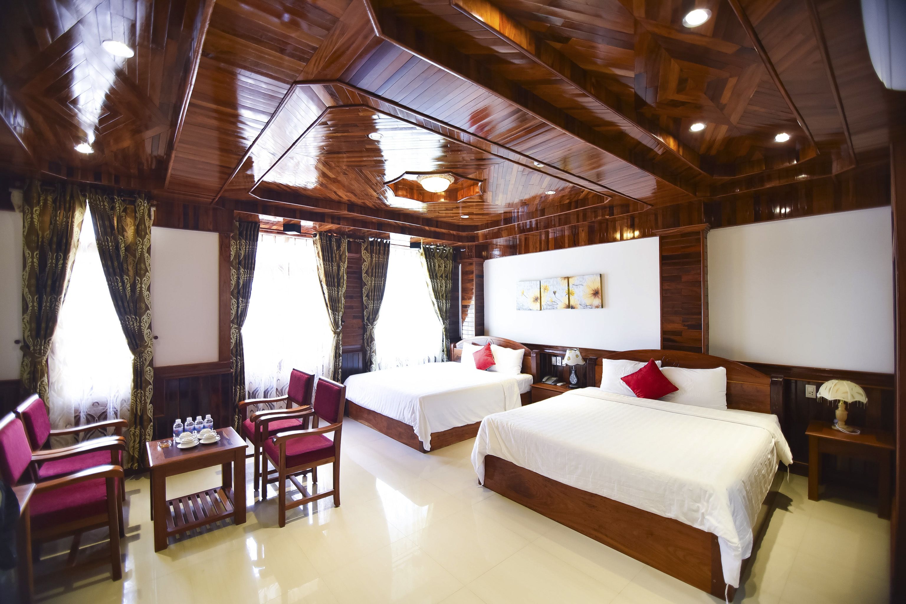A hotel room with two beds, a wooden ceiling, a table with chairs, and a fireplace.