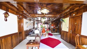 Un couloir d’hôtel avec des lambris en bois, une table centrale surmontée d’un chemin de table rouge et une horloge sur le mur de gauche.