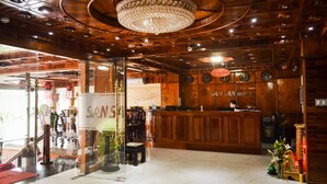 Un hall d’hôtel avec un comptoir d’accueil en bois, un lustre et une enseigne indiquant « HÔTEL SANSAN ».