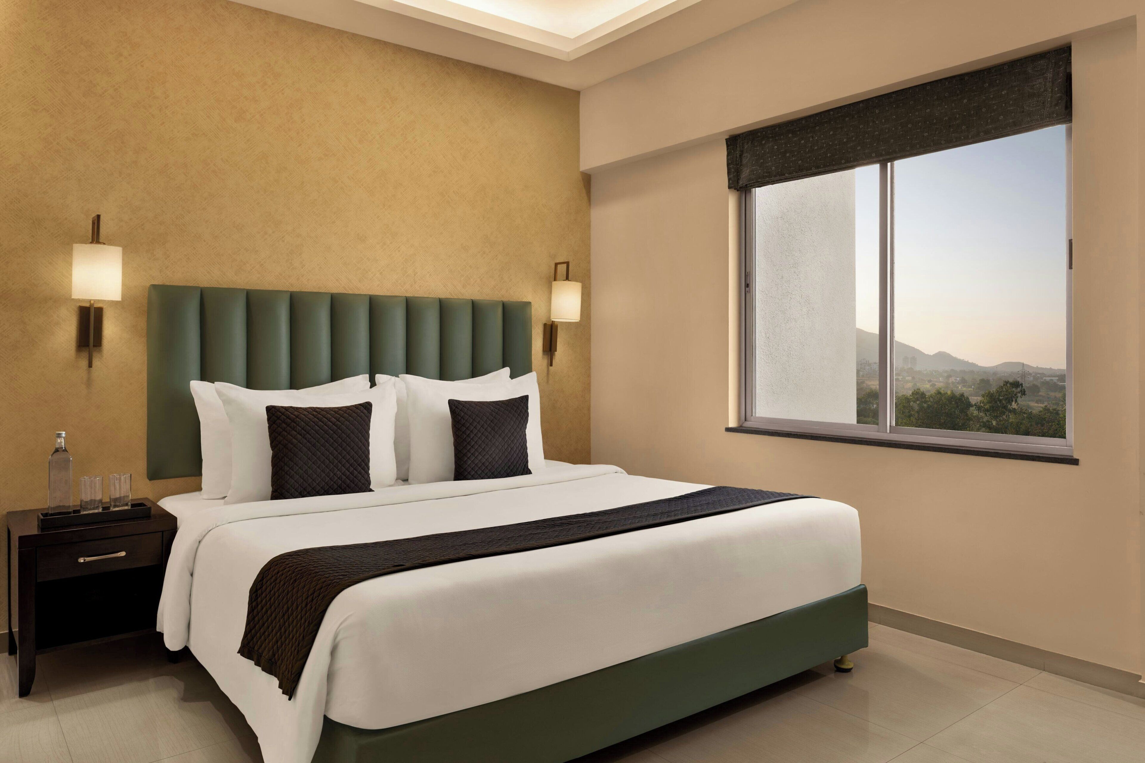 A hotel room with a large bed, two bedside tables, a window with a view, and wall-mounted lamps.