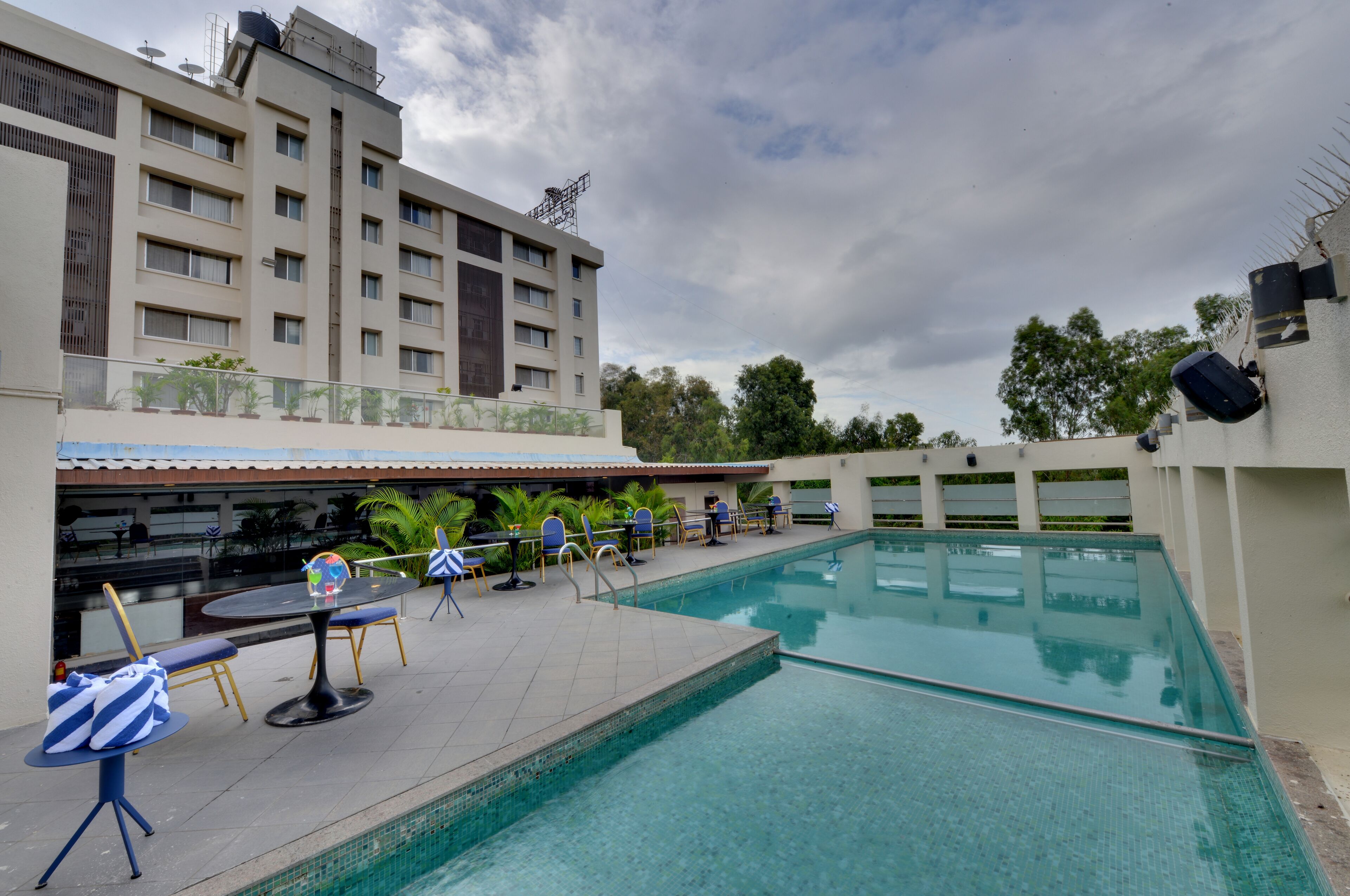 A swimming pool area with lounge chairs and tables, a covered seating area, and a building with multiple floors and balconies.