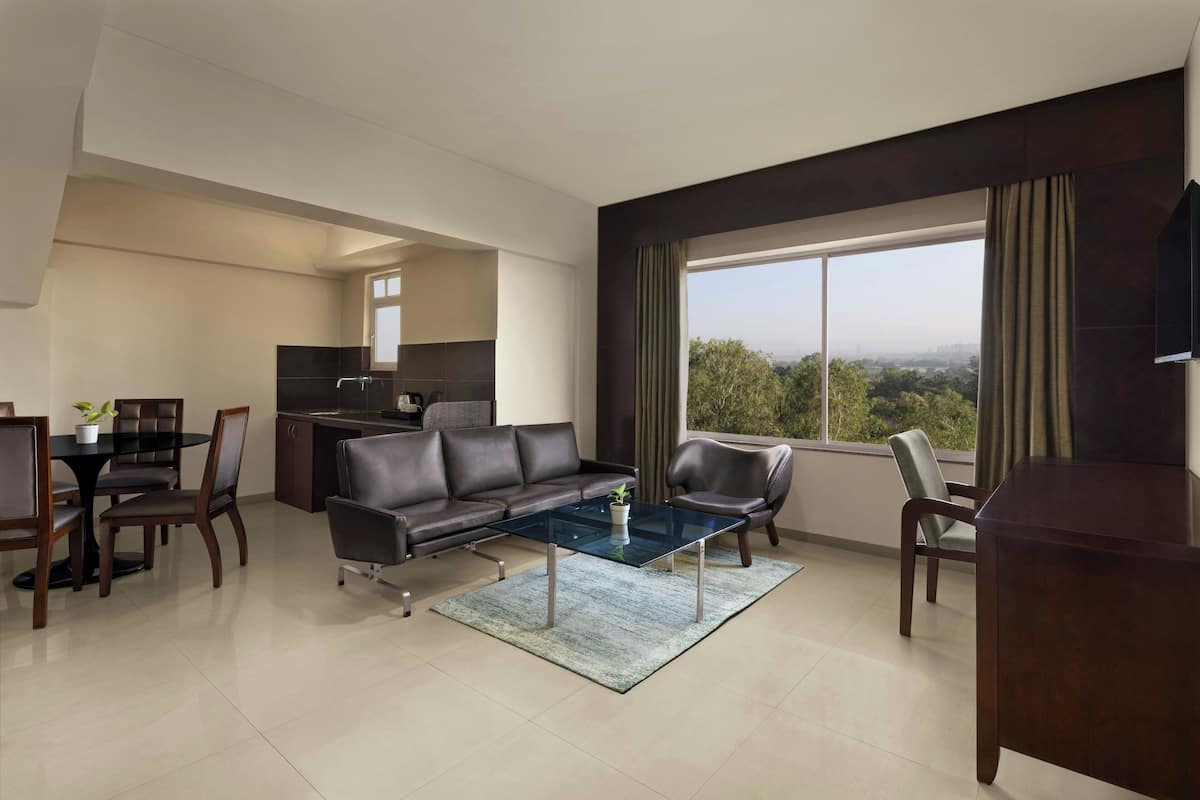 A modern living room with a glass coffee table, leather sofa, dining area, and a large window with a city view.