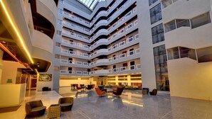 A modern hotel lobby with multiple floors, a central open space with seating, and a glass ceiling. - The Fern Residency Pune, Vadgaon-Talegaon, Series by Marriott (Mawal)