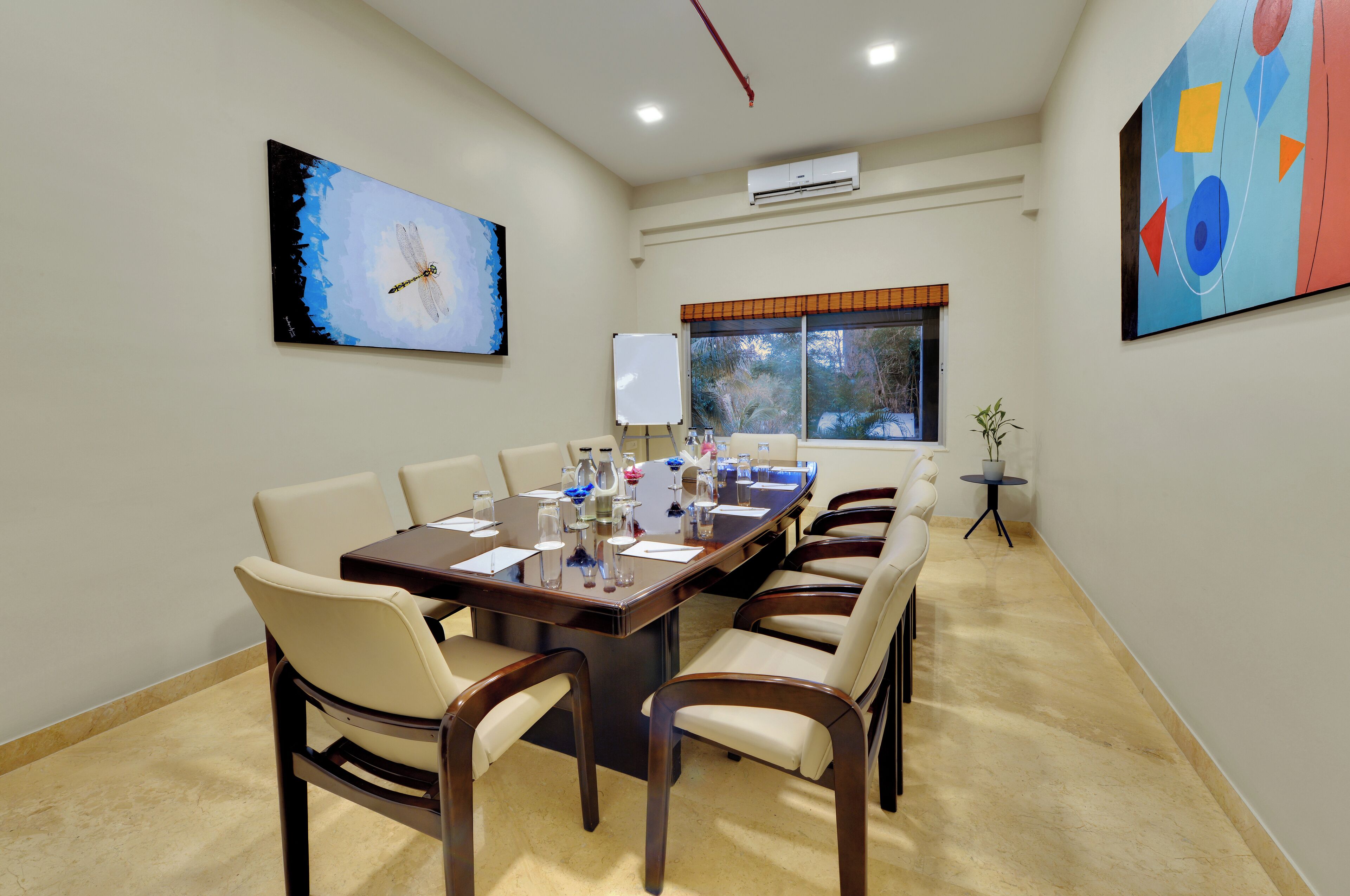 A conference room with a long table, six chairs, a whiteboard, and two paintings on the walls.