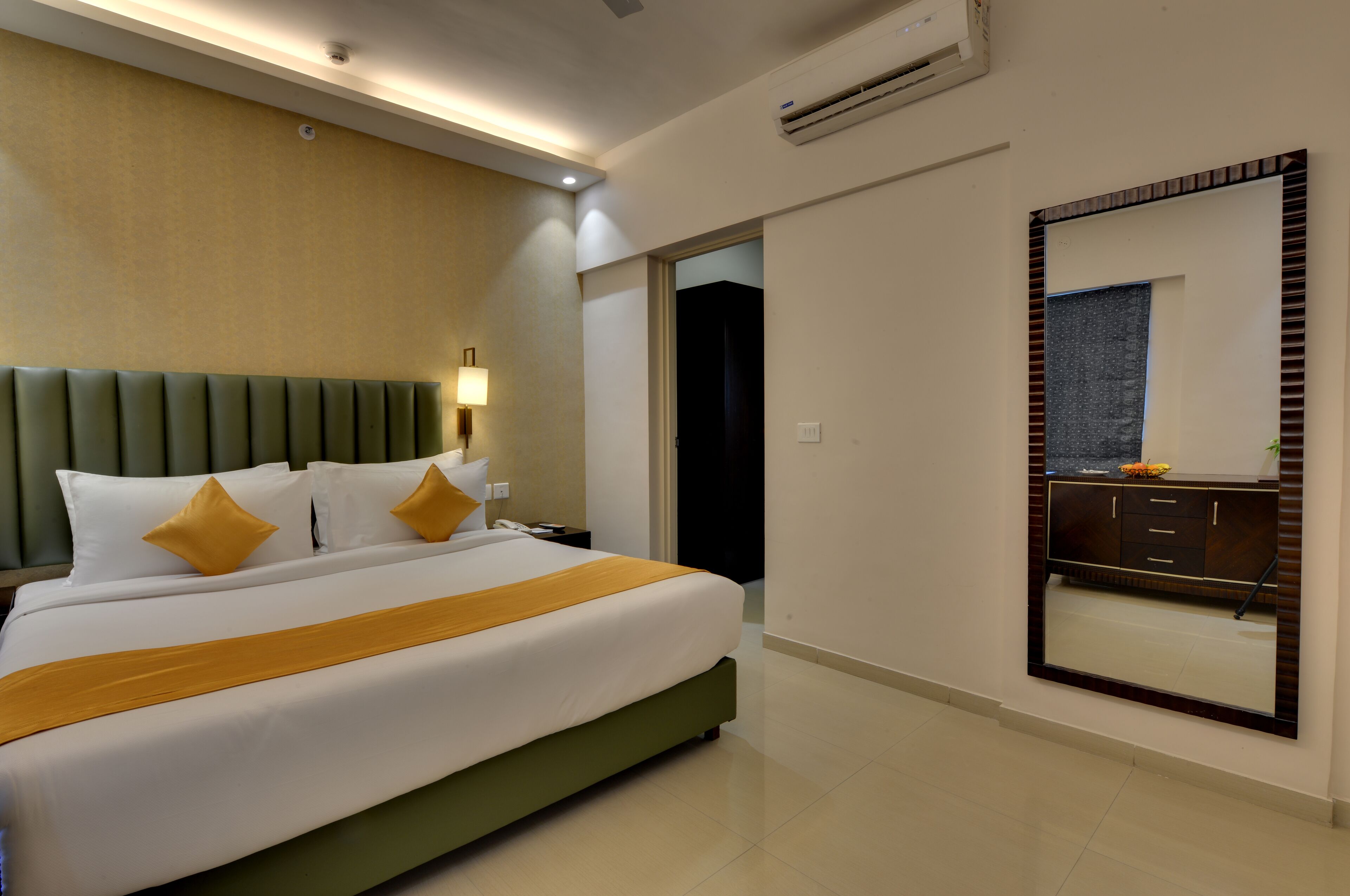 A hotel room with a large bed, a nightstand, a mirror, and a bathroom door.