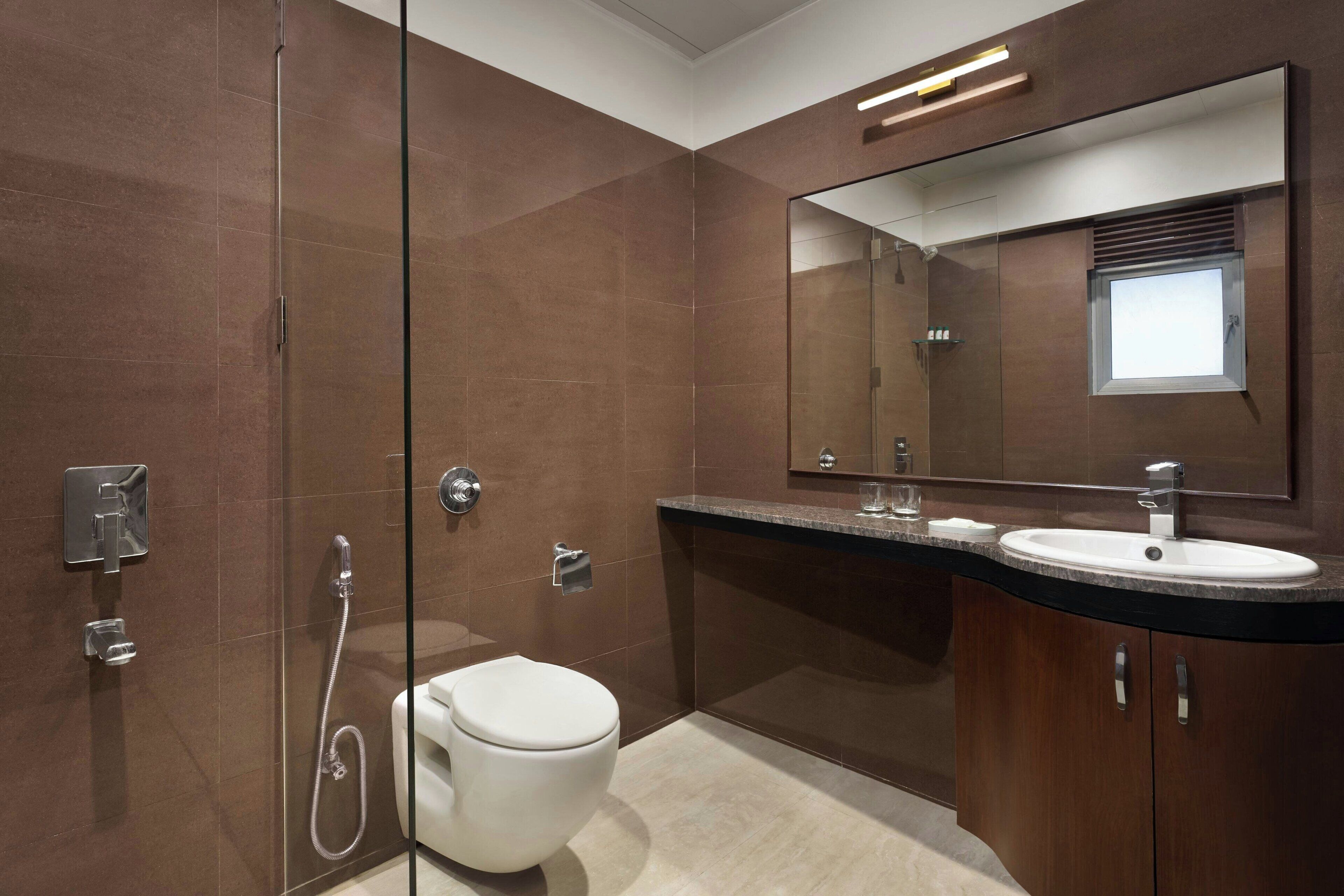 A modern bathroom with a glass shower enclosure, a white toilet, a sink with a mirror above, and wooden cabinetry.
