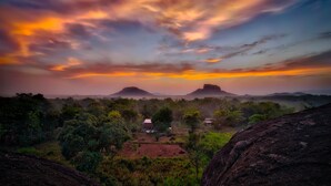 A landscape with a sunset, a small settlement, and mountains in the background. - Sigiri Choona Lodge (Sigiriya)
