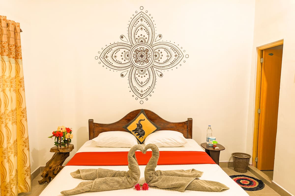 A hotel room with a bed, a decorative wall art, a wooden headboard, a nightstand, a vase with flowers, and a door.