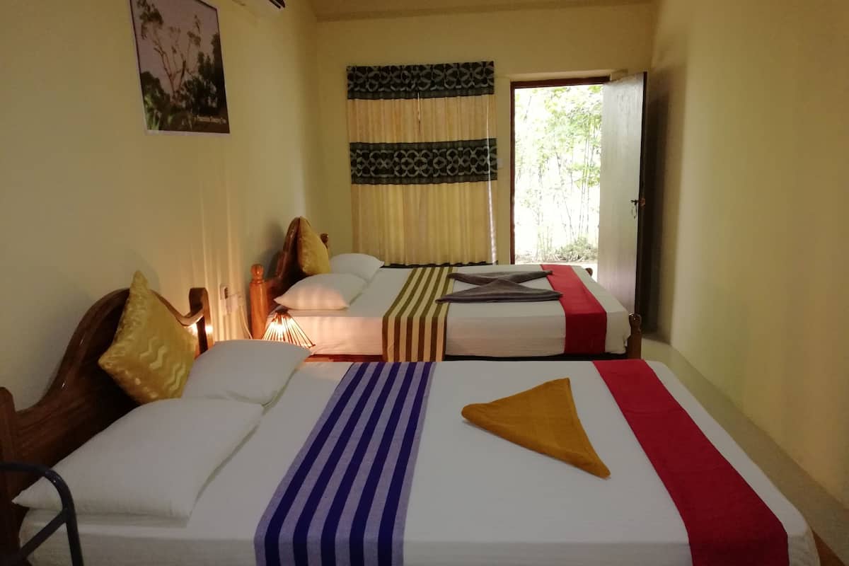 A hotel room with two beds, each with a different patterned bedspread. There is a window with curtains, a wall-mounted air conditioner, and a framed picture on the wall.