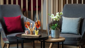 A modern living room with a grey sofa, a round table with drinks and snacks, and a potted plant. - Hostel by Randolins (St. Moritz)