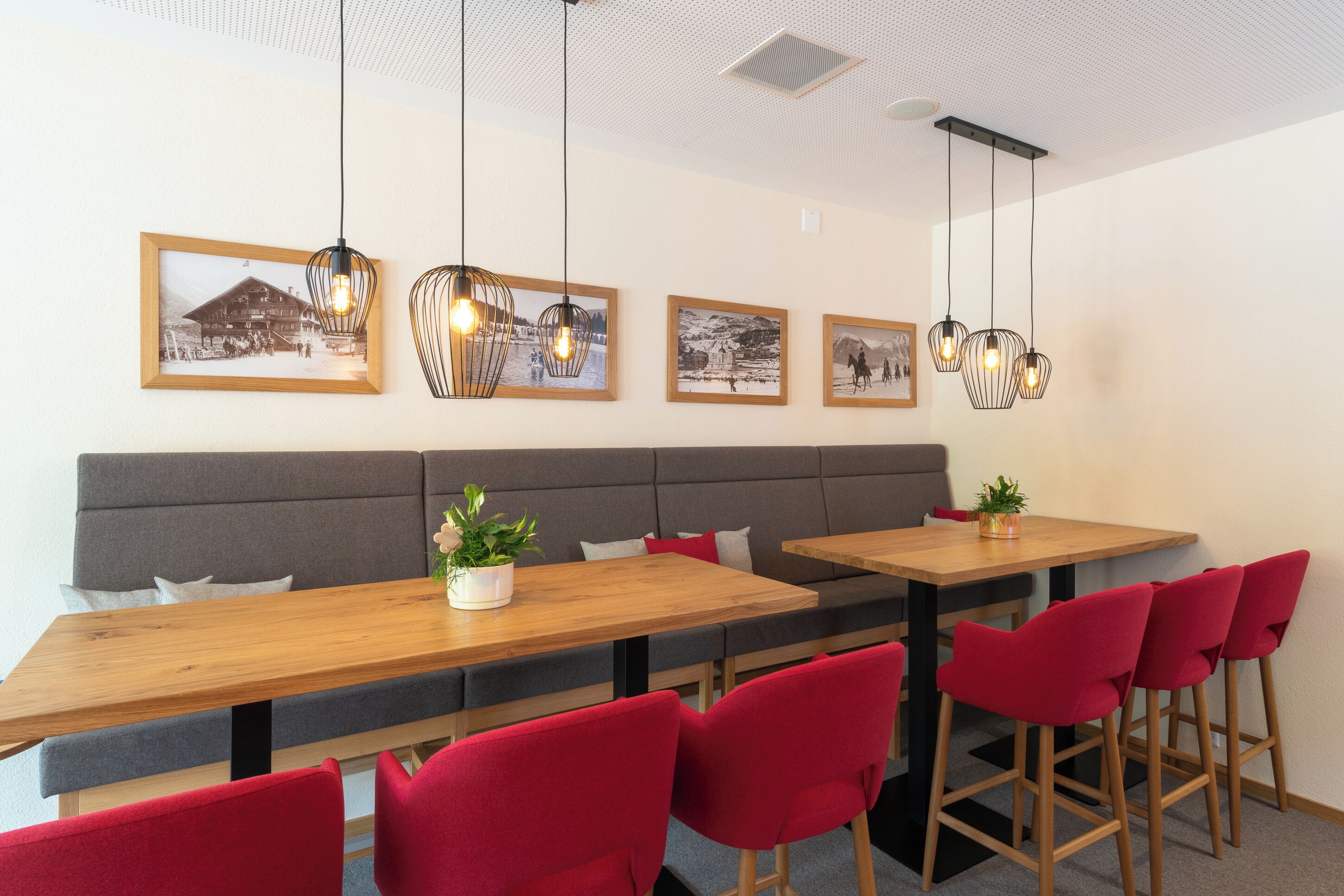 Un comedor moderno con mesas de madera, sillas rojas y fotografías enmarcadas en blanco y negro en la pared.