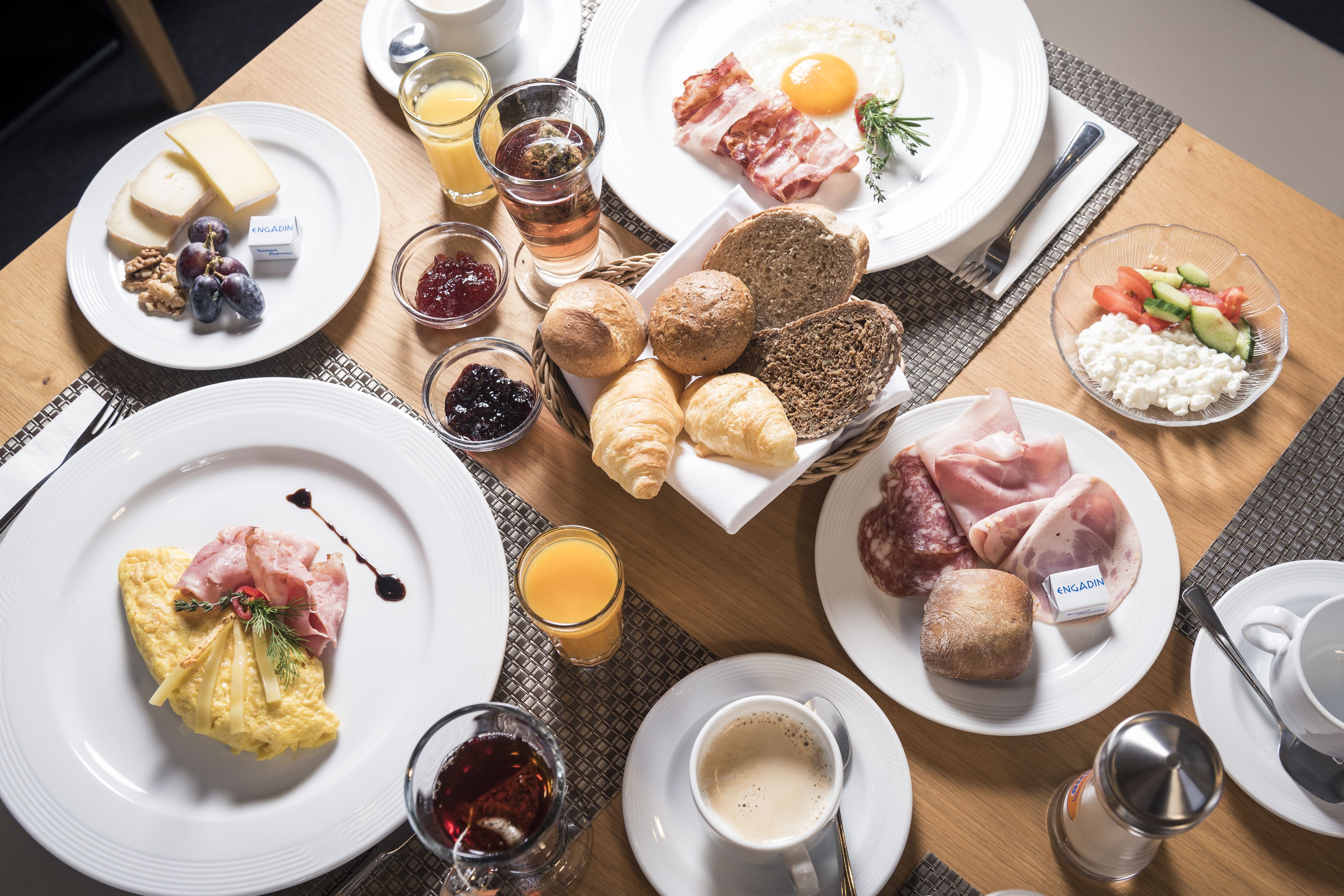 A breakfast table with various dishes including eggs, bacon, cheese, croissants, and fruits.