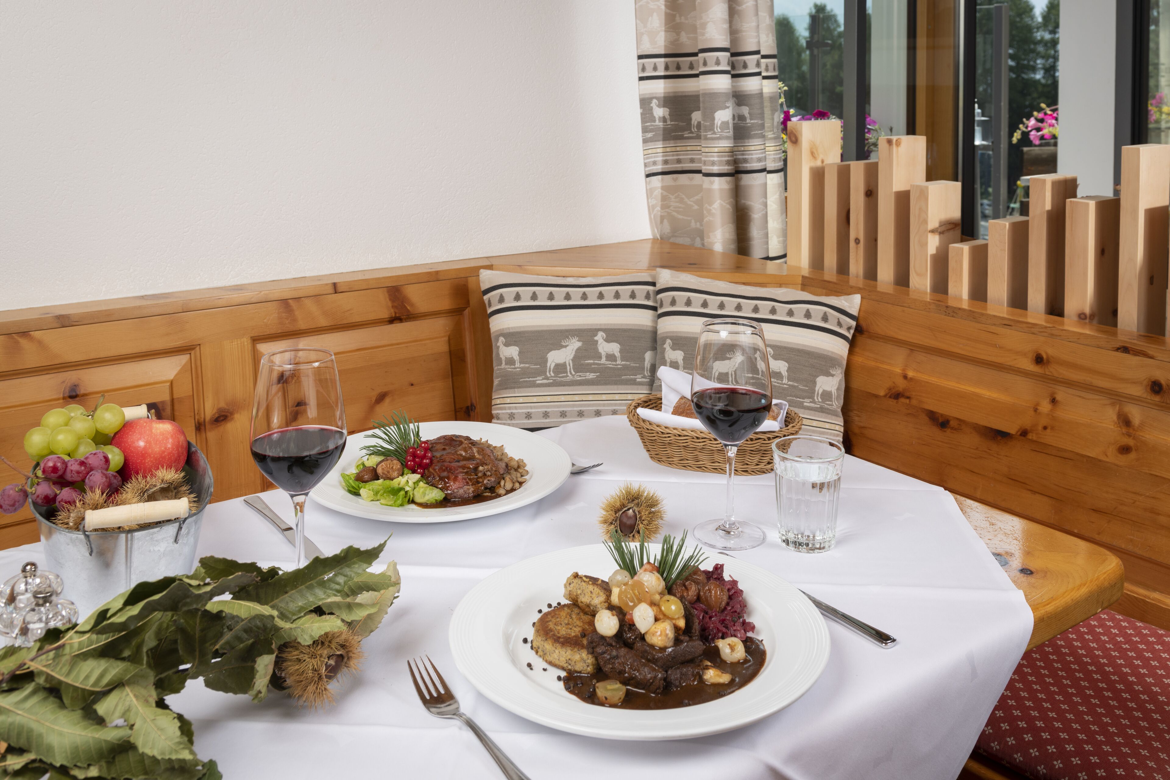 A dining table set with plates of food, glasses of wine, and a basket.