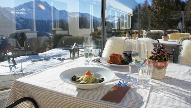 A table set for dining with a mountain view, a glass of water, and a decorative pinecone centerpiece. - Hostel by Randolins (St. Moritz)