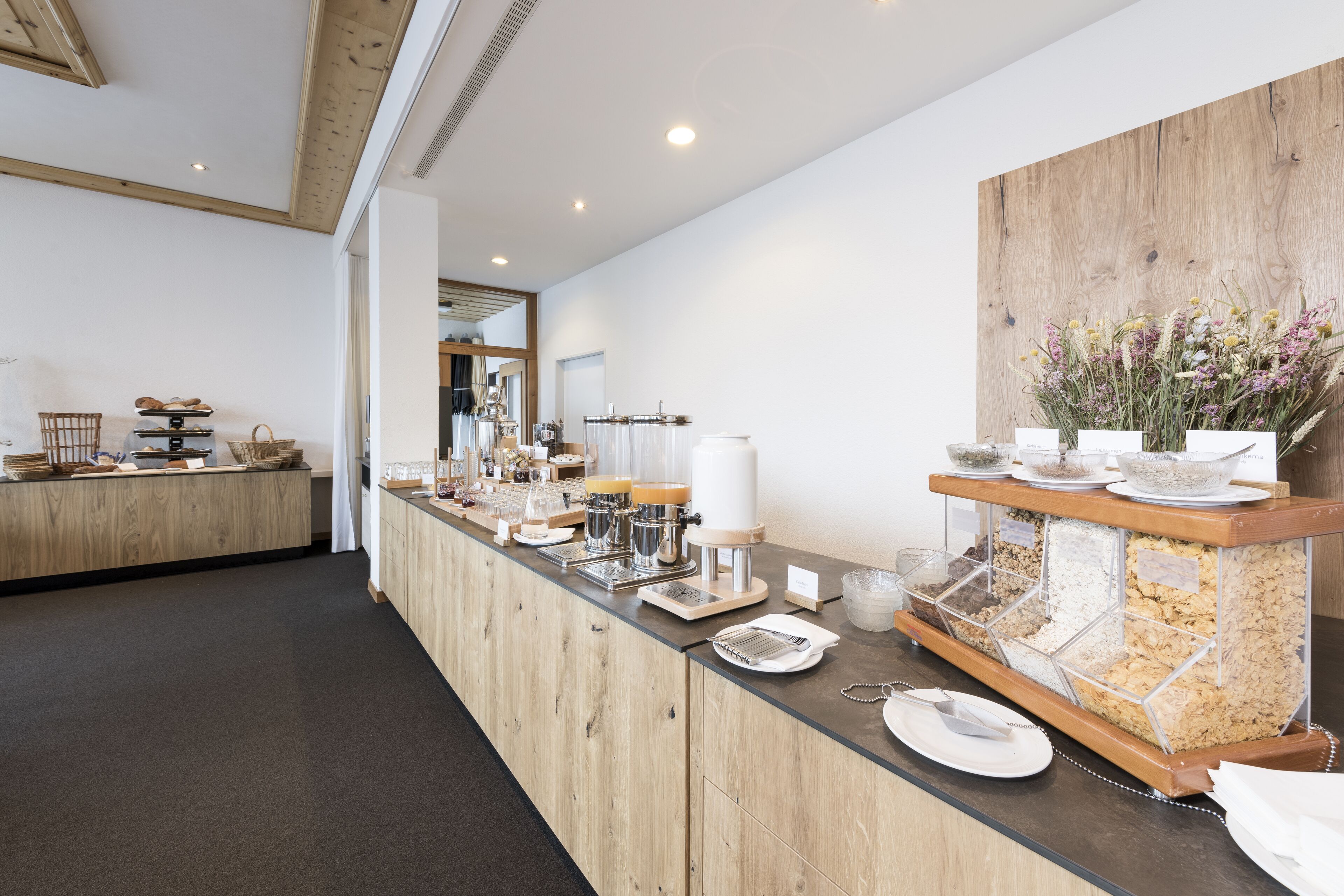 A buffet setup with a wooden counter, various food containers, and a decorative wall with flowers.