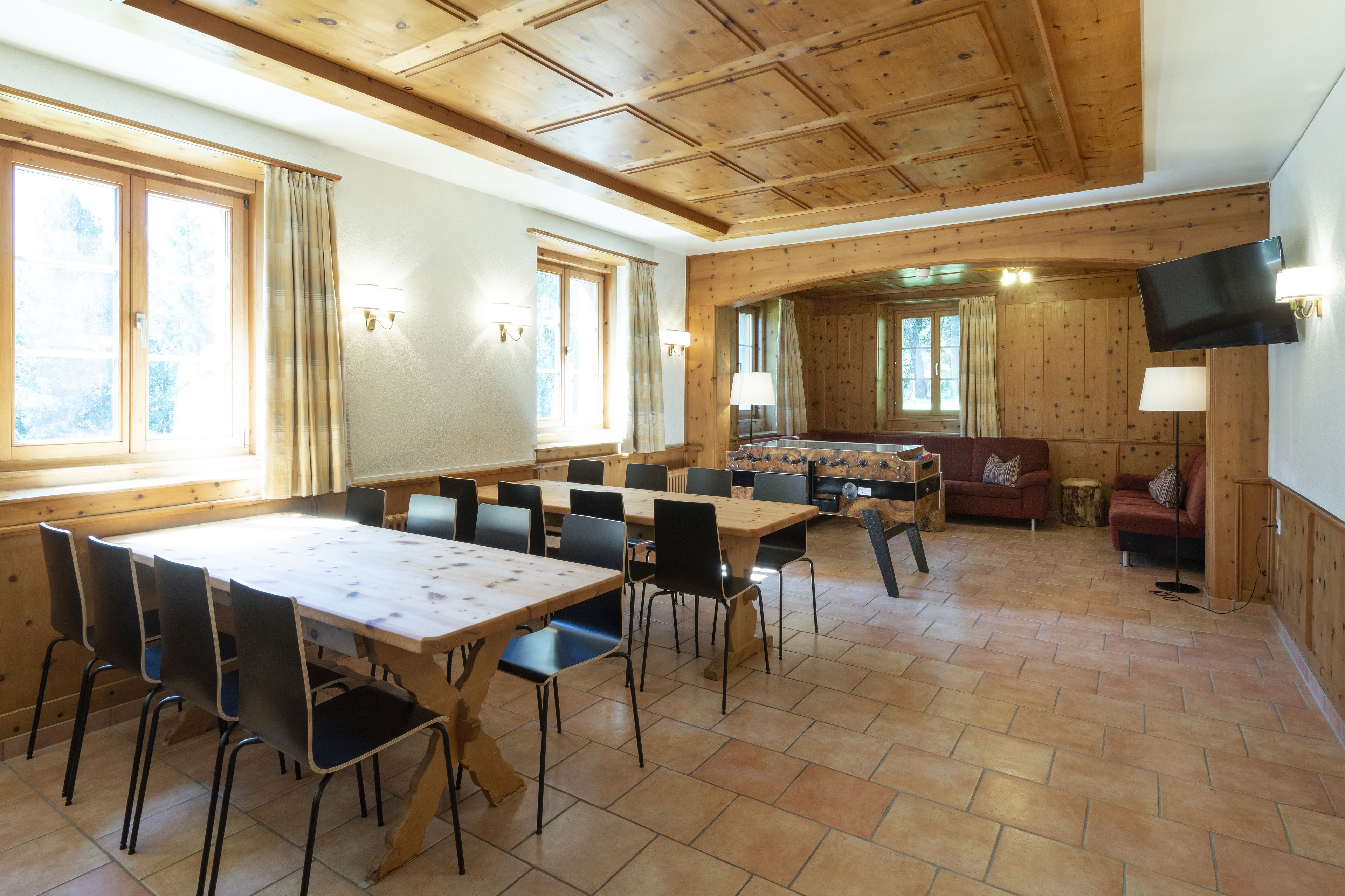 A dining area with a long table and chairs, a sofa, and a television mounted on the wall.