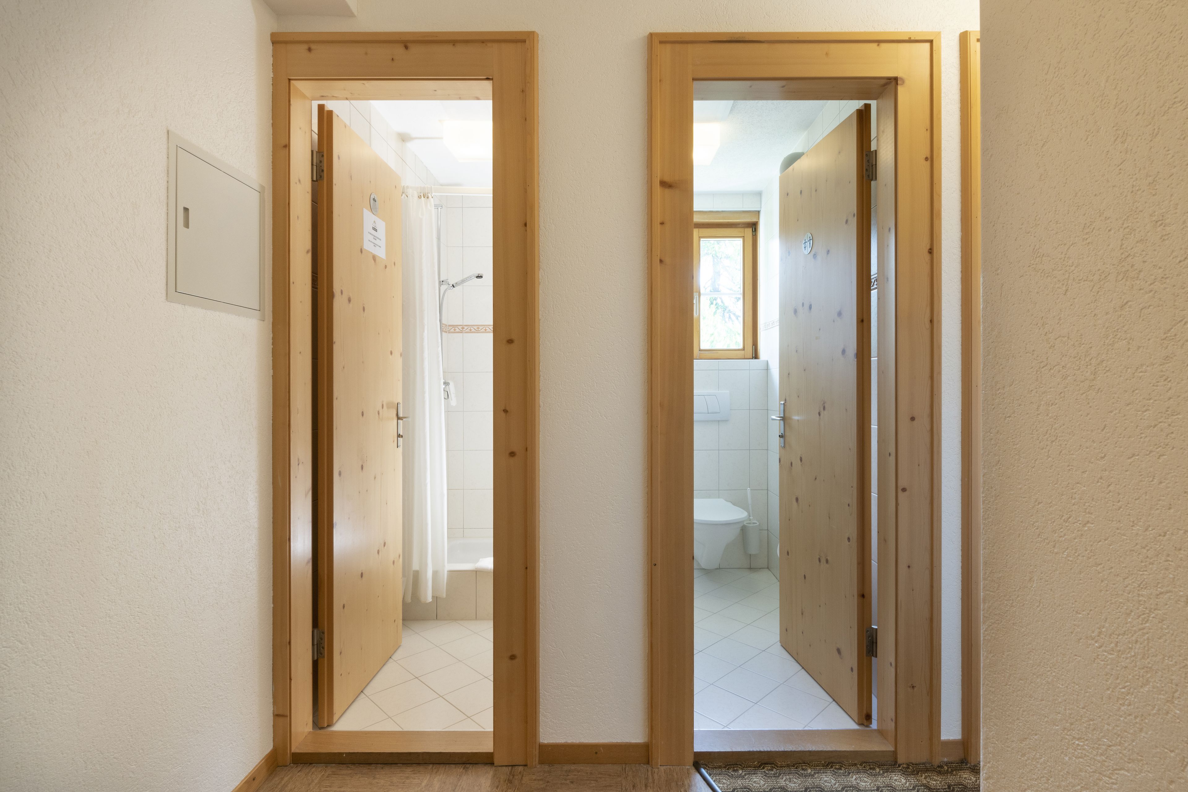 A hallway with wooden doors leading to a bathroom and a shower area.