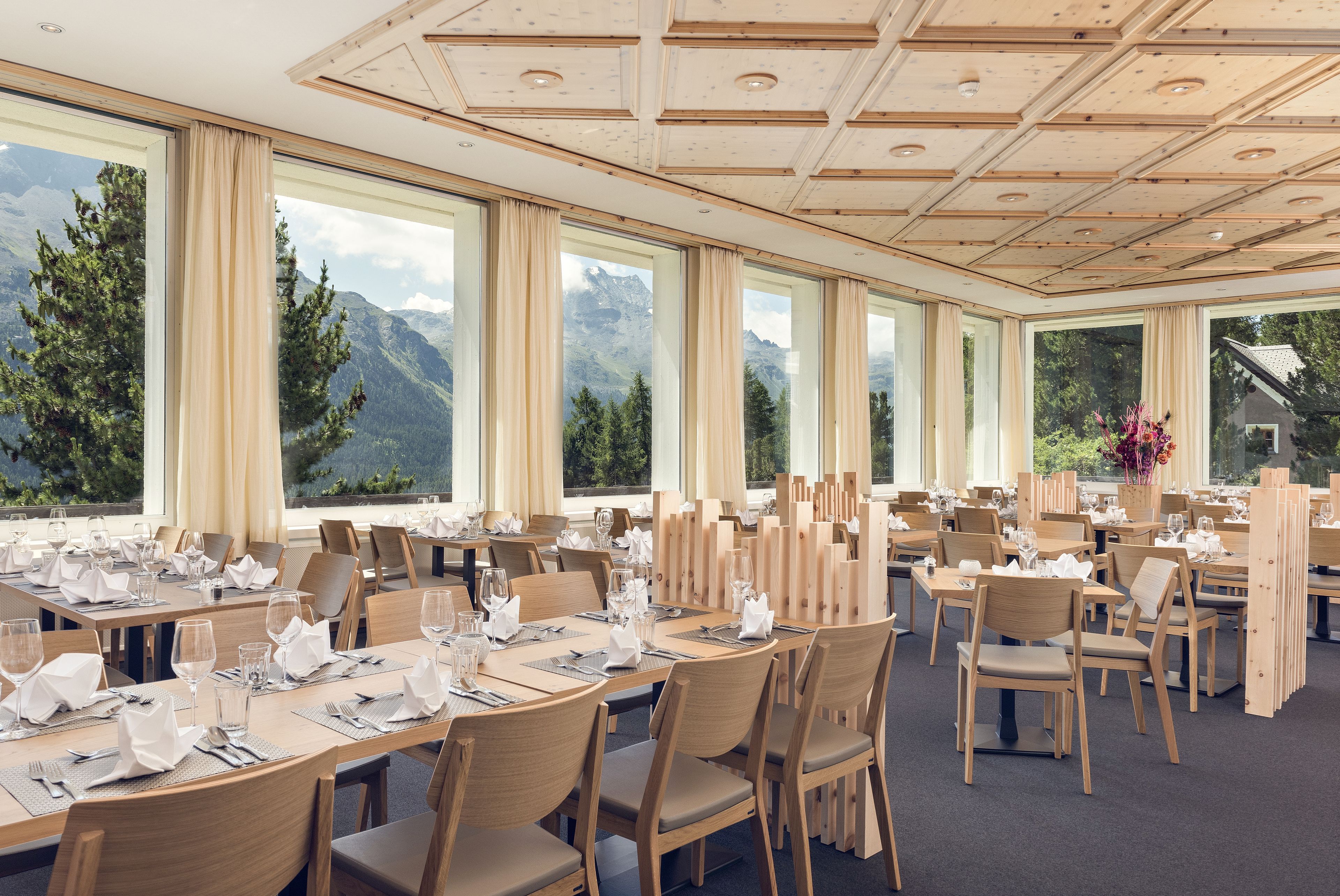 Un restaurante con varias mesas dispuestas para comer, amplias ventanas que ofrecen vistas a las montañas y un techo de madera.