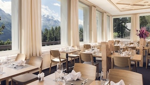 A restaurant with tables set for dining, large windows with mountain views, and a modern ceiling design. - Hostel by Randolins (St. Moritz)