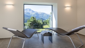 A balcony with two wicker chairs, a small table, and a view of mountains and trees. - Hostel by Randolins (St. Moritz)