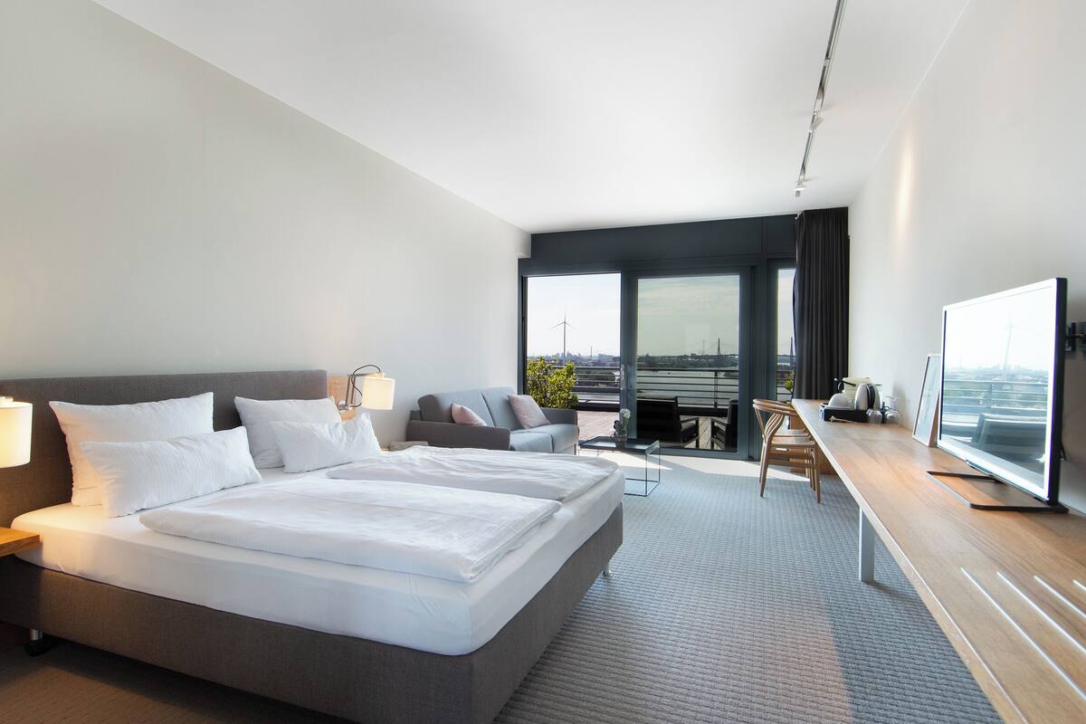 Une chambre d’hôtel moderne dotée d’un grand lit, d’un canapé, d’un bureau avec une télévision et offrant une vue sur la ville.