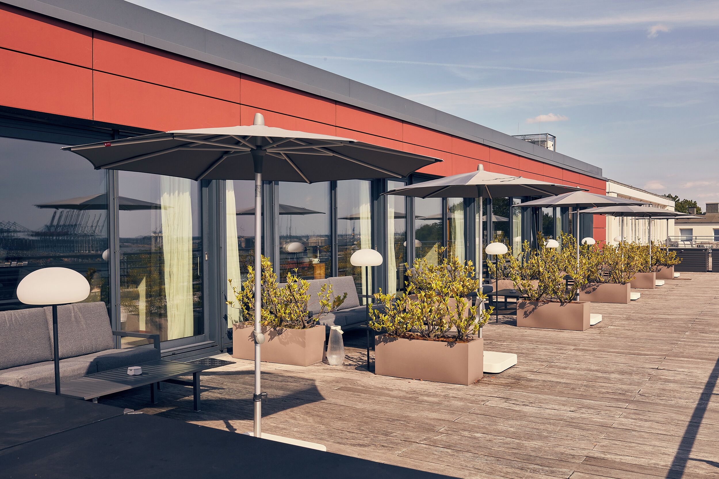 Eine Dachterrasse mit Sitzgelegenheiten, Pflanzgefäßen und Sonnenschirmen.