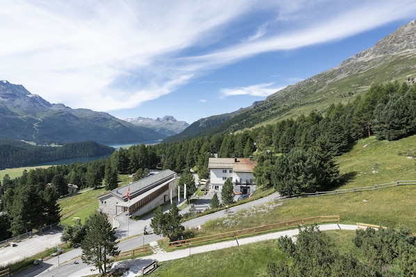 A mountain landscape with a building surrounded by trees and a lake. - Randolins Familienresort (St. Moritz)