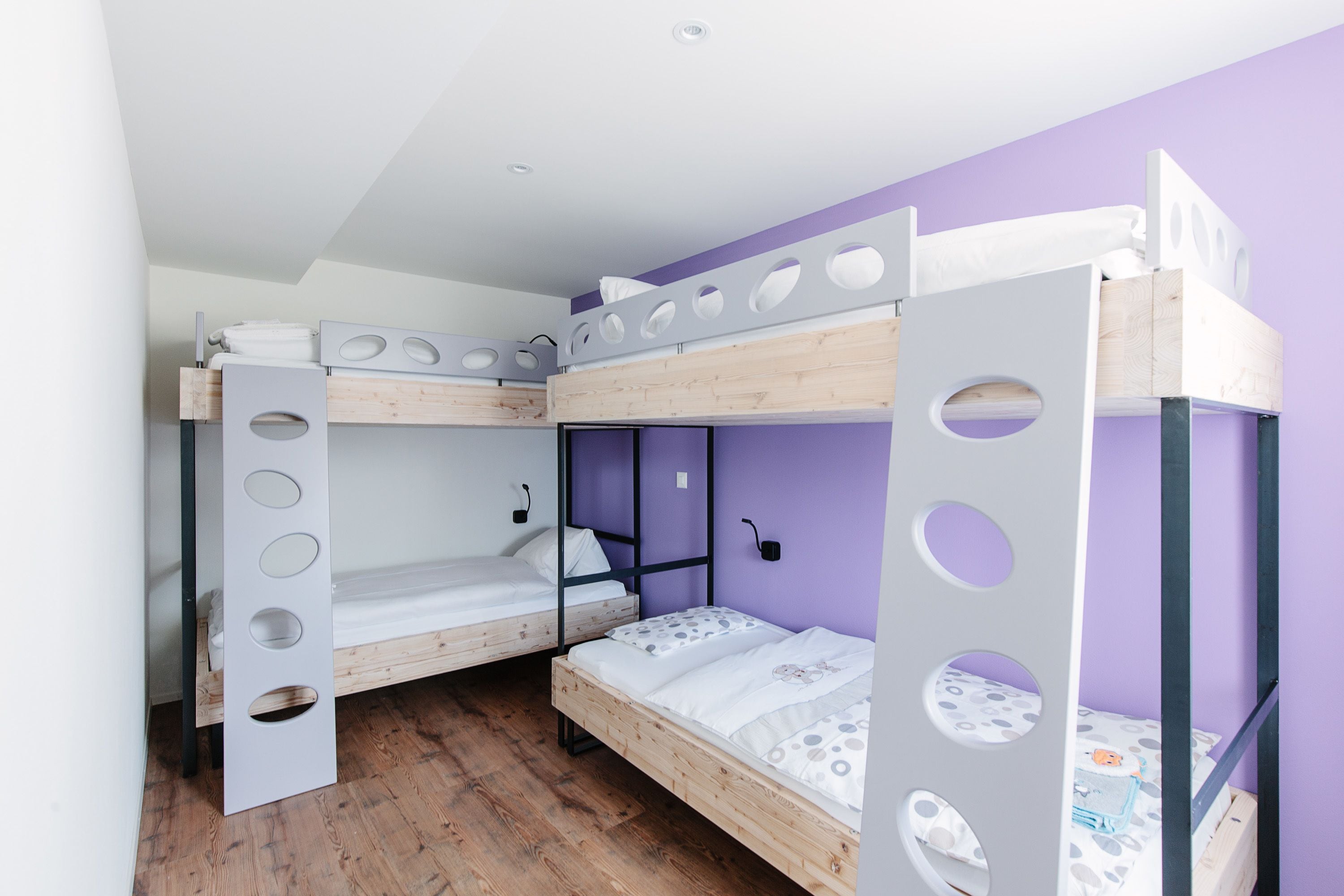 A bunk bed room with a purple wall, wooden flooring, and a white ceiling.