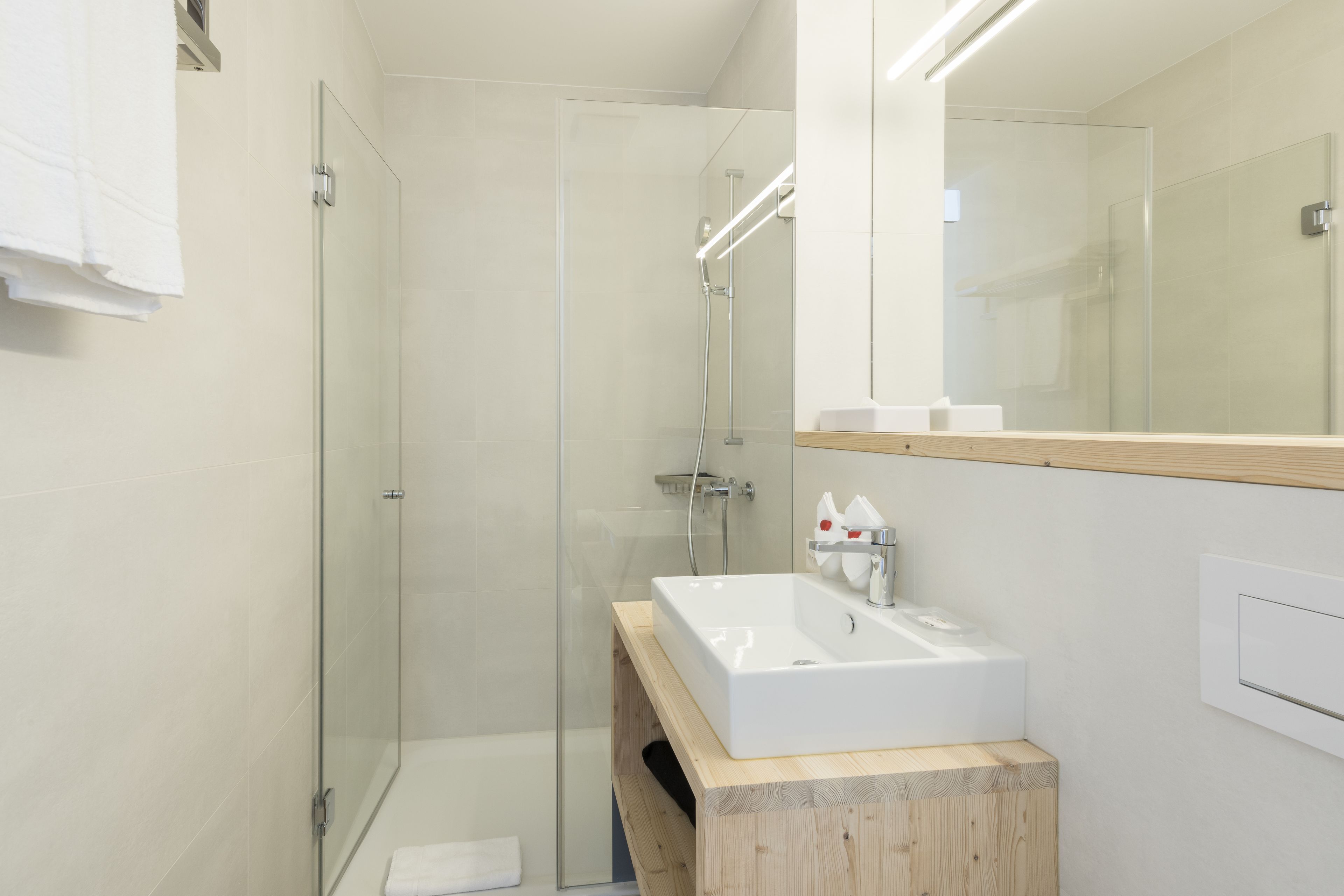 A modern bathroom with a glass shower enclosure, a white sink, and a wooden vanity.
