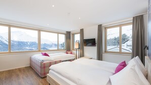 Habitación de hotel con dos camas, televisión y ventanas amplias con vista a la montaña.