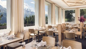 Un restaurante con mesas dispuestas para comer, amplias ventanas con vistas a la montaña y un diseño moderno de techo.